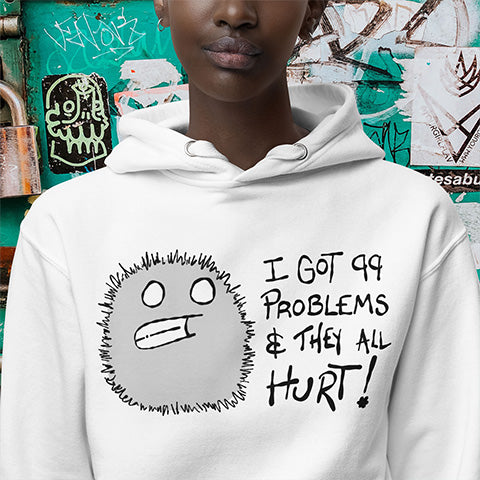 Person wearing a white hoodie with a graphic design and text in front of a graffiti-covered wall.