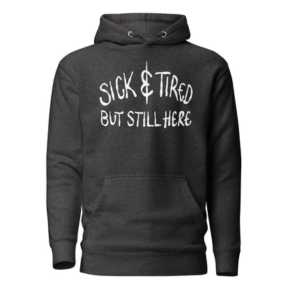 Black hoodie with white text 'SICK & TIRED BUT STILL HERE' on a white background